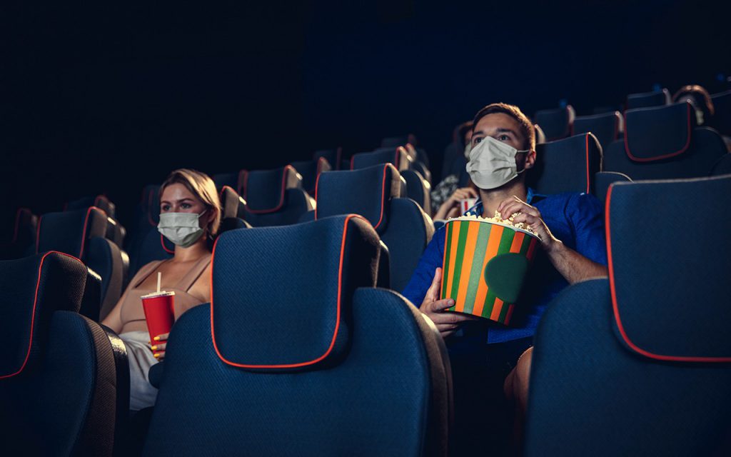 ชายหญิงกำลังนั่งชมภาพยนตร์ในโรง ผู้ชายหยิบข้าวโพดคั่ว ส่วนผู้หญิงถือแก้วน้ำอัดลม